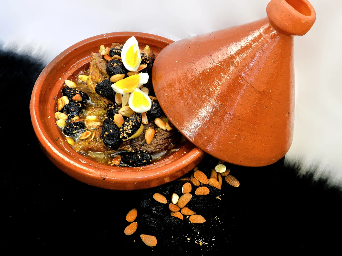 A Moroccan lamb tagine with prunes, almonds and quail eggs in a terracotta dish with its conical lid beside it